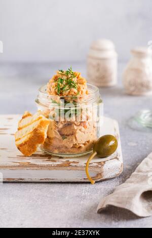 Delizioso pate di pollo fatto in casa con spezie e aneto in un vaso di vetro e una fetta di pane nelle vicinanze e cappero su uno sfondo chiaro. Messa a fuoco selettiva Foto Stock