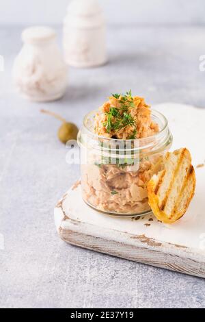 Delizioso pate di pollo fatto in casa con spezie e aneto in un vaso di vetro e una fetta di pane nelle vicinanze e cappero su uno sfondo chiaro. Messa a fuoco selettiva Foto Stock