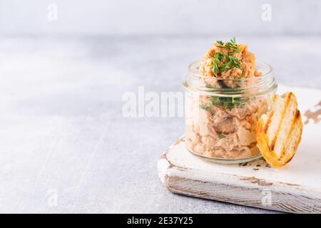 Delizioso pate di pollo fatto in casa con spezie e aneto in un vaso di vetro e una fetta di pane nelle vicinanze e cappero su uno sfondo chiaro. Messa a fuoco selettiva Foto Stock