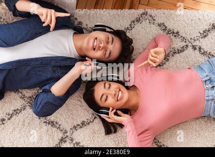 Coniugi asiatici che indossano cuffie ascolto di musica sdraiata al piano interno Foto Stock