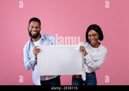 Felice coppia nera che tiene banner bianco con spazio vuoto su sfondo rosa studio, mockup per il tuo design Foto Stock