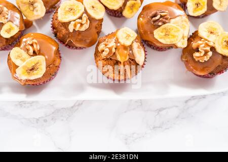 Fresco cucinato banana nut bread muffin spruzzata con fatti in casa caramello, decorate con noci e banana chips. Foto Stock