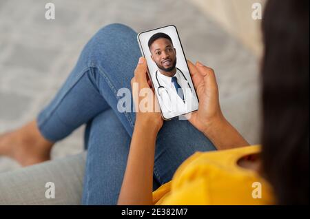 Concetto di telemedicina. Irriconoscibile Black Lady con smartphone, facendo videoconferenza con Doctor Foto Stock