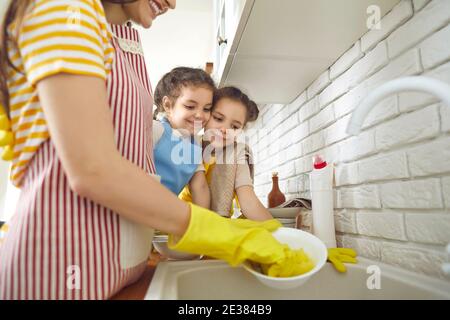 Due ragazze imparano a fare le faccende domestiche e a guardare la madre lavare i piatti dopo pranzo Foto Stock