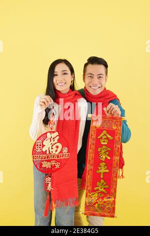 Felice giovane coppia asiatica in abiti invernali mostrando Lunar New Decorazioni dell'anno con l'iscrizione dei migliori auguri Foto Stock