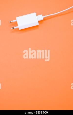 Un'immagine verticale del caricabatteria USB isolato su sfondo arancione Foto Stock