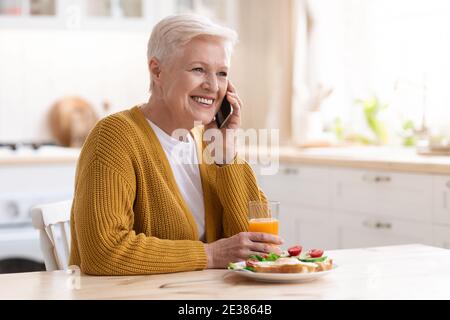 Nonna allegra che ha una telefonata mentre mangia a casa Foto Stock