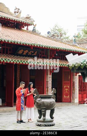 Calma giovane coppia buddista vietnamita che prega all'urna di rame con bastoni per fumare al tempio buddismo Foto Stock