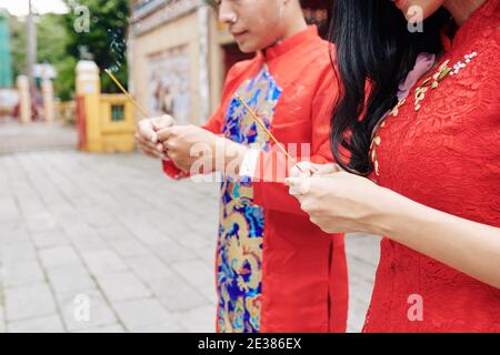 Immagine ritagliata della giovane coppia vietnamita che prega nel tempio insieme con bastoni per fumare nelle mani Foto Stock