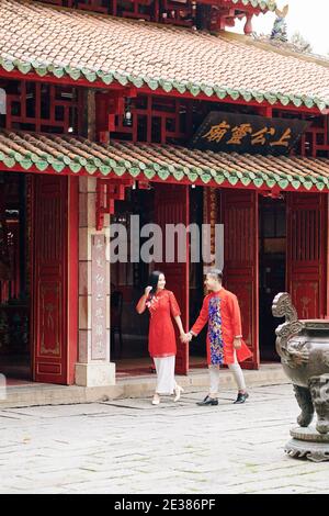 Felice appena sposato coppia asiatica in abiti tradizionali che tengono le mani quando si cammina all'aperto nella città vecchia Foto Stock