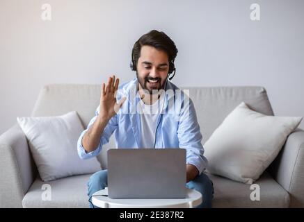 Videochiama l'uomo orientale con il laptop e le cuffie A casa Foto Stock