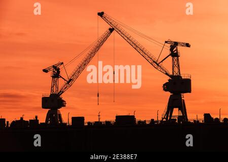 Le gru portuali si stagliano sul cielo rosso del tramonto, foto del trasporto industriale Foto Stock