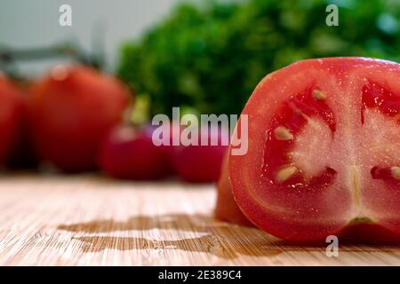 Primo piano di un pomodoro appena tagliato a metà arrangiato tra lattuga verde e ravanelli sani Foto Stock