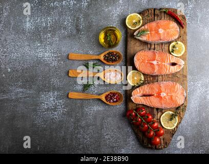 tre trote crude di pesce bistecca, salmone e spezie su tavola di legno, sfondo scuro Foto Stock