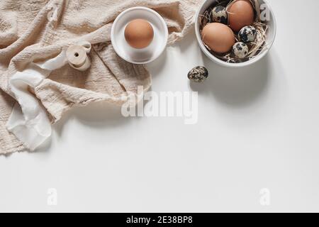 Cornice decorativa pasquale, banner. Primavera ancora vita con quaglia naturale e uova di gallina, ciotole in ceramica e tovaglioli di lino isolati su sfondo bianco tavolo Foto Stock