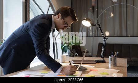 Primo piano uomo d'affari sicuro indossare occhiali scrivere note sugli adesivi Foto Stock