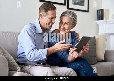 Felice coppia anziana matura che usa un tablet digitale seduto sul divano di casa. Foto Stock