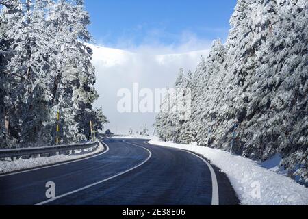 Solitaria e tortuosa strada in un paesaggio di montagna innevato in una soleggiata giornata invernale. Concetto di fuga in auto. Viaggio su strada. Foto Stock