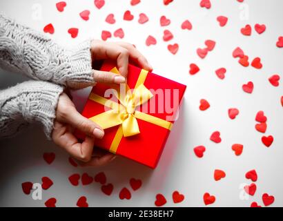 le mani tengono un regalo su uno sfondo bianco con cuori rossi. Foto Stock