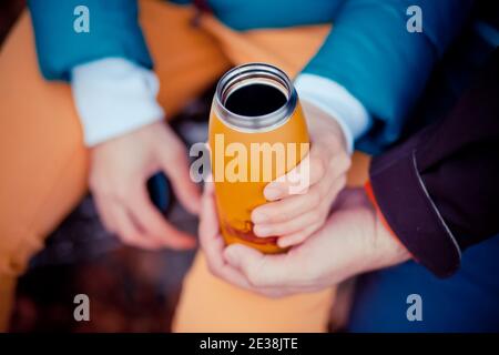 Thermos arancio nelle mani di un uomo. Foto Stock