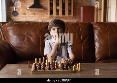 Il ragazzino intelligente gioca a scacchi pensando a casa Foto Stock