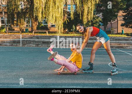 Due ragazze teen, amici che si divertono con uno skateboard. Una ragazza spinge l'altra da dietro Foto Stock