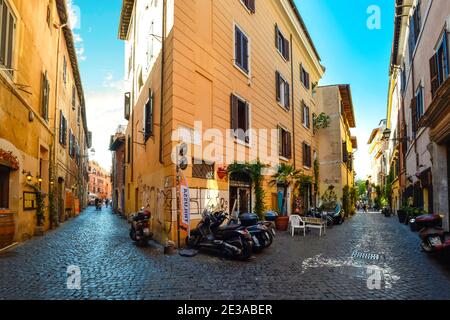 Pittoresca e colorata strada acciottolata con moto parcheggiate e negozi nel quartiere Trastevere di Roma. Foto Stock