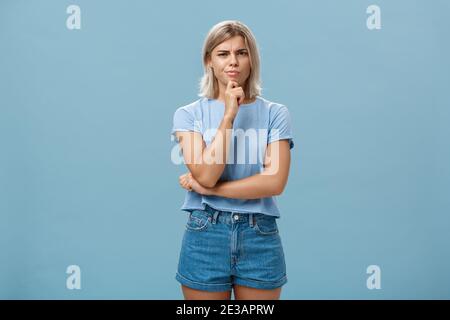 Dubito che sia una buona idea. Sospetto intenso creativo giovane collega femminile in outdoor outfit che si accigliano da pensieri dubbi tenendo la mano sul mento mentre Foto Stock