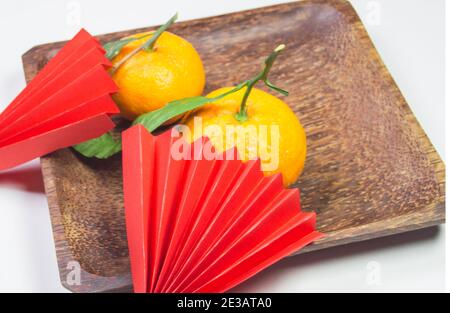 Capodanno cinese, composizione con mandarini, carta origami rosso tifosi su un piatto di legno scuro su sfondo bianco. Foto Stock