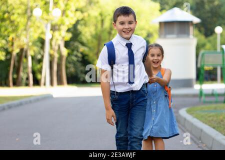 Allegro scolari ragazza e ragazzo in una camicia bianca con zaini al mattino in una giornata di sole in estate Foto Stock