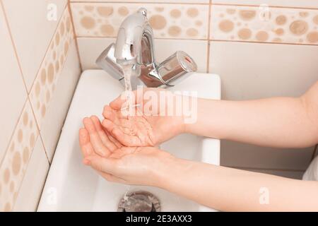 Due mani di bambino sopra il lavandino con acqua di versamento Foto Stock