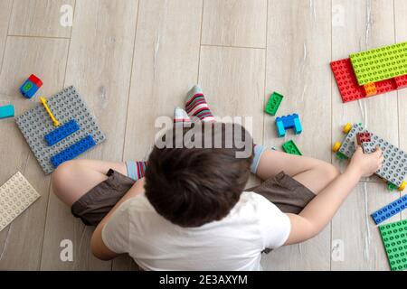 Gioco di ragazzo con costruttore di plastica multicolore sul pavimento in camera. Vista dall'alto Foto Stock