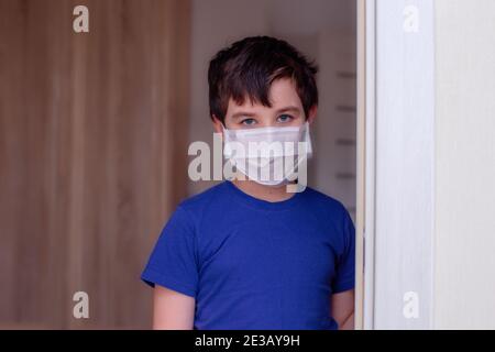 Bruna ragazzo in abiti blu e bianco maschera medica stand nella porta Foto Stock