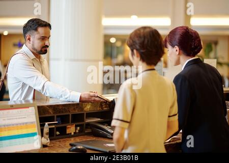 Uomo serio che mostra le informazioni di prenotazione sullo smartphone al manager all'indirizzo reception dell'hotel Foto Stock