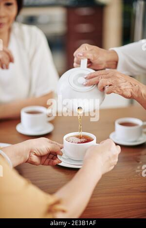 Immagine ravvicinata della donna anziana che versa il tè nero caldo tazze per le sue amiche Foto Stock