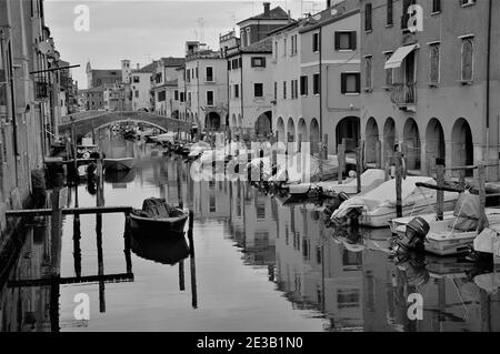 Foto in bianco e nero di canale, barche e case Riflettendo sull'acqua a Chioggia nella laguna veneta Foto Stock