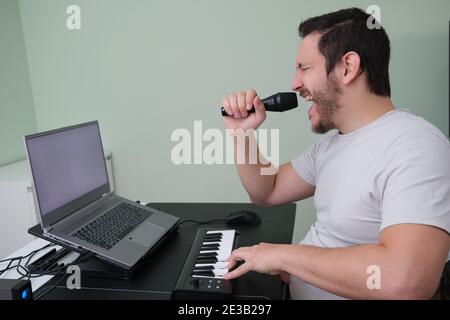 Un blogger uomo, youtuber, influencer che registra un video che riproduce il pianoforte elettronico e canta a casa. Musicista, cantante, pianista. Schermo bianco o Foto Stock