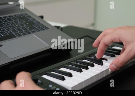 Mani che suonano il pianoforte elettronico davanti al computer portatile. Imparare a suonare il pianoforte. Foto Stock