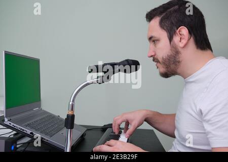 Un uomo che impara a suonare il pianoforte elettronico su internet a casa. Schermo verde sul computer portatile. Foto Stock