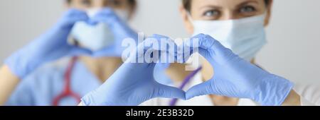 Due medici in maschere mediche e guanti di gomma che mostrano il cuore con le mani Foto Stock