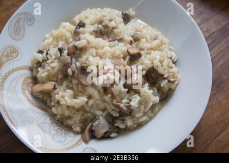 Risotto ai funghi, piatto di riso cotto con fette di funghi comuni in un recipiente bianco Foto Stock