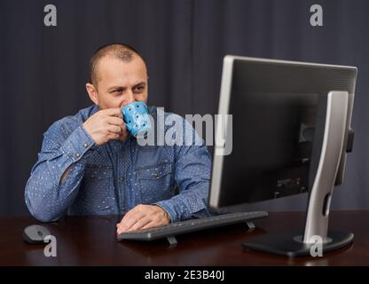 Uomo d'affari alla sua scrivania con il suo computer che beve una tazza di cofee o tè Foto Stock
