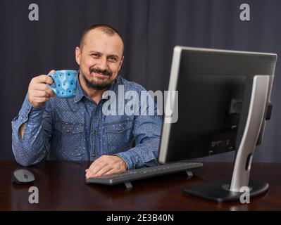 Uomo d'affari alla sua scrivania con il suo computer che beve una tazza di cofee o tè Foto Stock