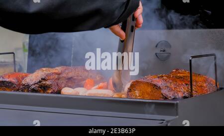 Primo piano: Chef grigliare salsicce e carne di maiale su braciere al festival alimentare Foto Stock