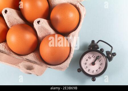 Uova di gallina in un cartone di uovo e sveglia nera Foto Stock