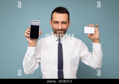 Bell'uomo giovane fresco felice bello da indossare casual elegante vestiti in piedi isolati sopra parete colorata di sfondo che tiene lo smartphone e. Foto Stock