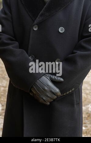 Primo piano della parte del corpo del maschio, in piedi all'aperto. Corpo di uomo irriconoscibile in camice nero e guanti in pelle nera. Foto Stock