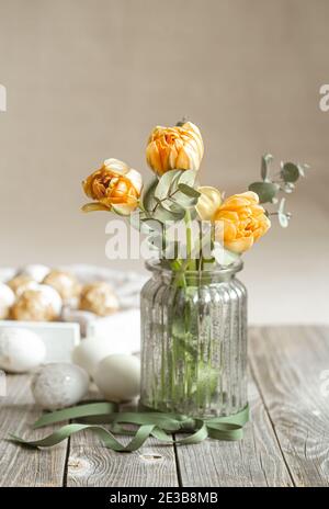 Un bouquet di fiori in vaso di vetro con elementi decorativi su sfondo sfocato. Concetto di vacanza di Pasqua. Foto Stock