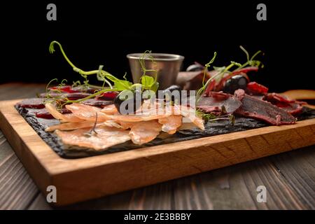 Salumi, salsicce, basturma, affumicati, con salsa e olive, su tavola di legno, su fondo ligneo Foto Stock