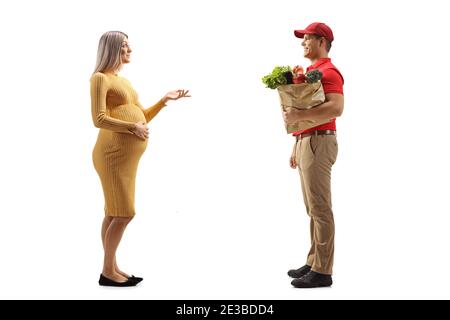 Foto di profilo a lunghezza intera di una donna incinta che parla con un corriere con una borsa della spesa isolata su sfondo bianco Foto Stock